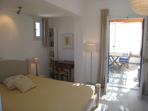 A bedroom with a bed, a desk, a chair, and a balcony with a table and chairs. - Naxos Beachvilla, a dreamhouse, 60m to sandy beach, big garden, top location (Naxos Town)