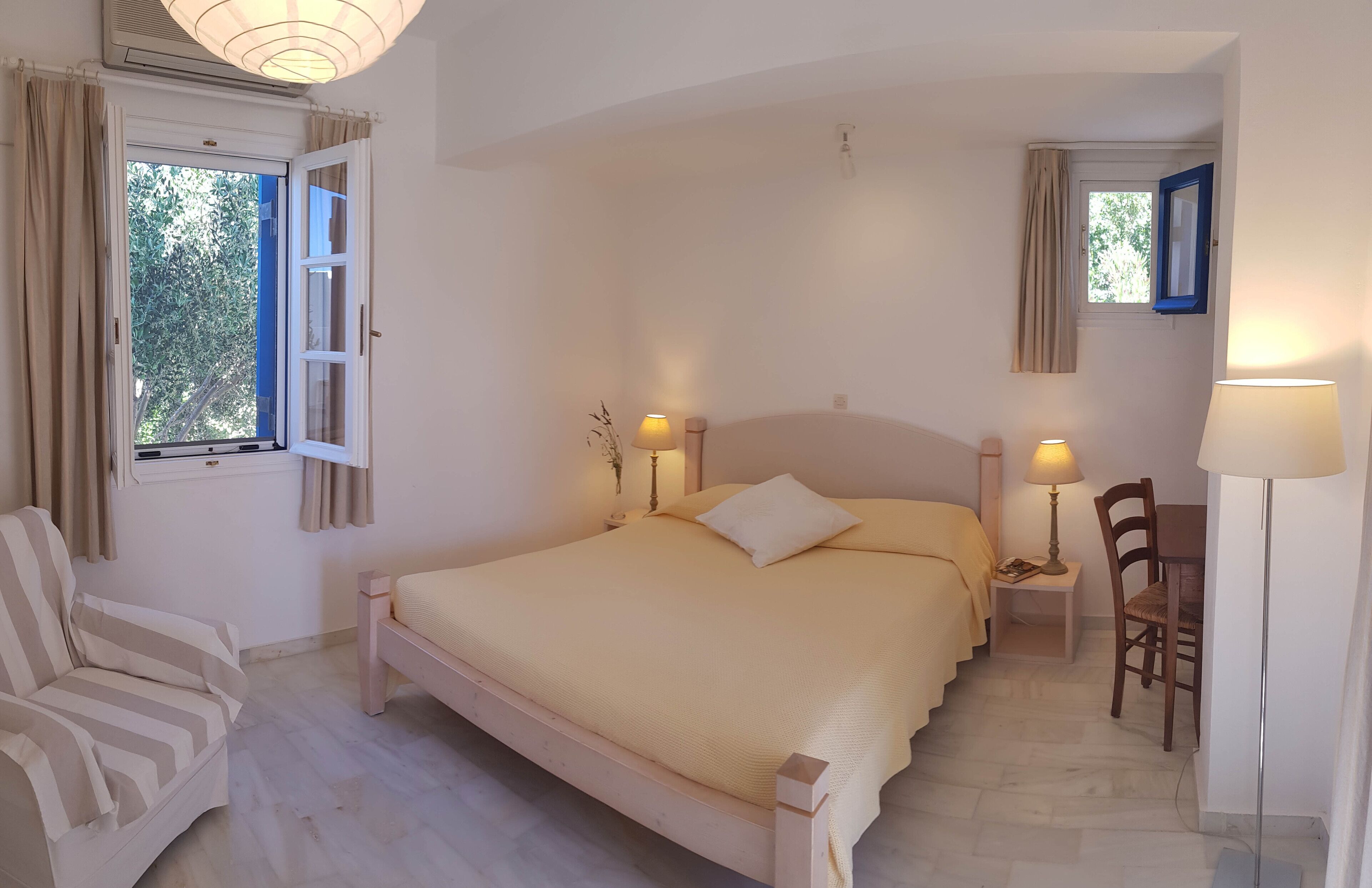 Une chambre à coucher comprenant un lit, des tables de chevet, une chaise, un bureau et une lampe.