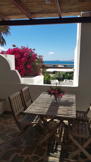 An outdoor patio with a table and chairs, a view of the sea, and pink flowers. - Naxos Beachvilla, a dreamhouse, 60m to sandy beach, big garden, top location (Naxos Town)