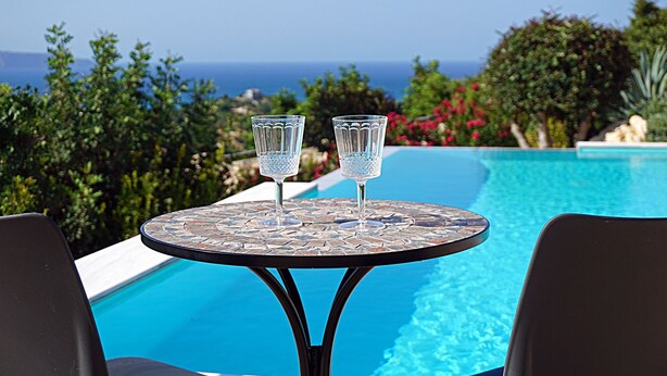A round table with two clear glasses and a view of a swimming pool and ocean.