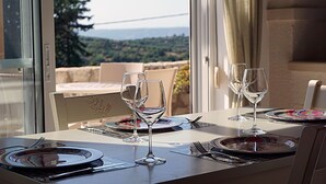 A dining table with two wine glasses and plates, set against a scenic view of hills and a bridge.
