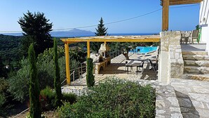 A stone patio with outdoor furniture, a pergola, and a view of a blue pool and ocean.