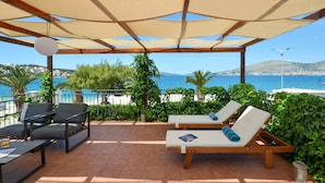 Un espace extérieur aménagé, abrité et doté de deux fauteuils et d’une table, offrant une vue sur une plage et la mer.