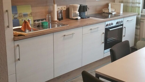 Et moderne køkken med hvide skabe, en træbordplade, kaffemaskine og komfur.