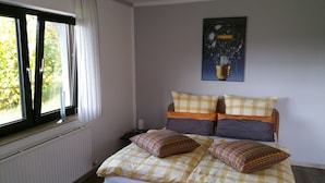 Et soveværelse med seng, et vindue med gardiner, en radiator og en lampe på væggen.