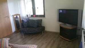 Et værelse med trægulv, en sofa, et fjernsyn og et vindue med udsigt til træer.