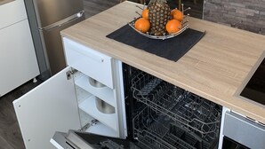 Ett kompakt kök med en inbyggd diskmaskin, ett litet kylskåp och en matplats med bord och stolar.