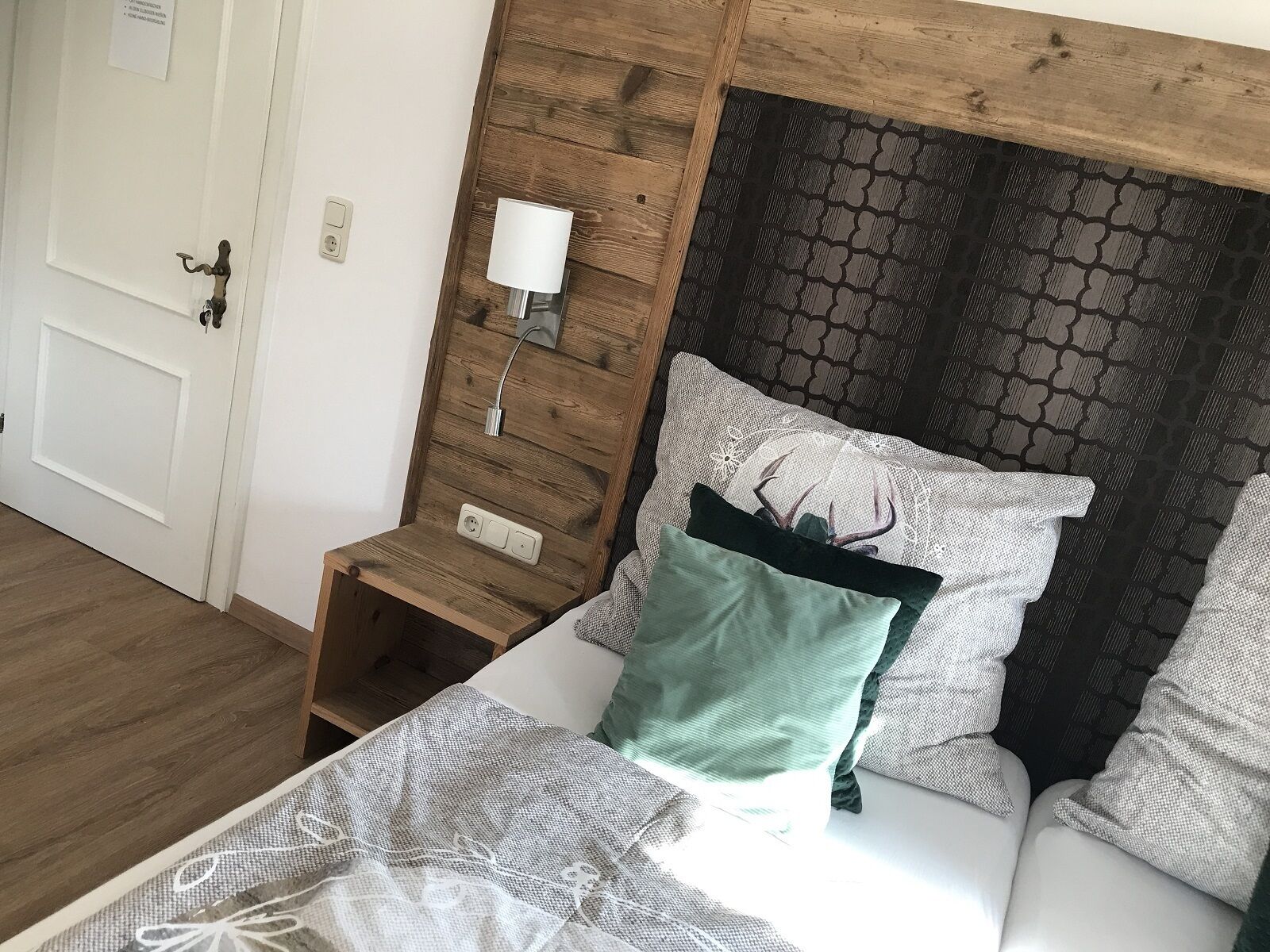 A room with a wooden headboard, a bedside table with a lamp, and a bed with patterned bedding.