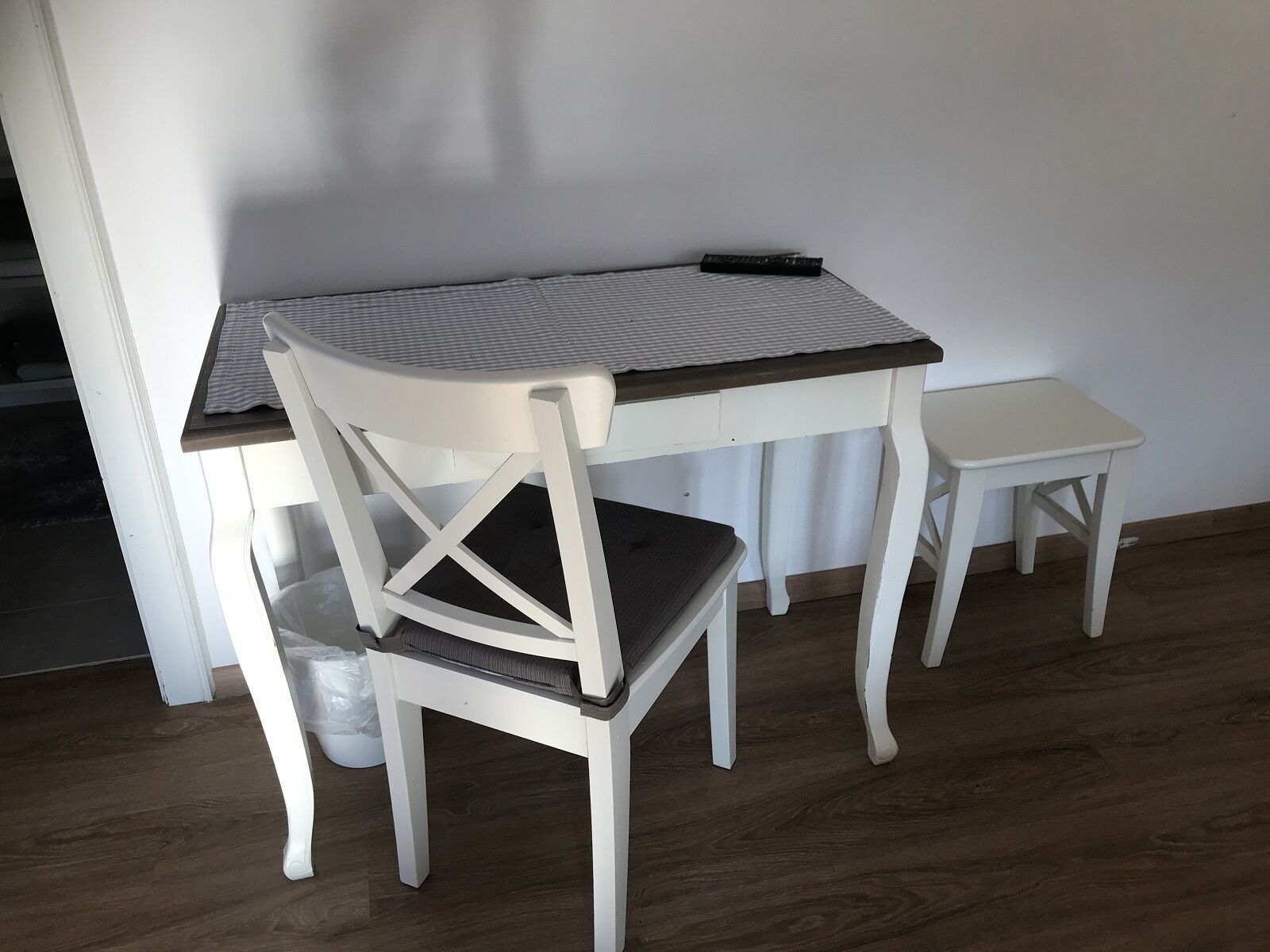 Une petite table de salle à manger en bois, de couleur blanche, recouverte d’une nappe à rayures, et accompagnée de deux chaises assorties.