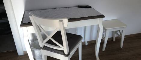 Une petite table de salle à manger en bois, de couleur blanche, recouverte d’une nappe à rayures, et accompagnée de deux chaises assorties.