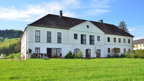Un edificio grande y blanco con techo oscuro, rodeado por un campo verde exuberante.