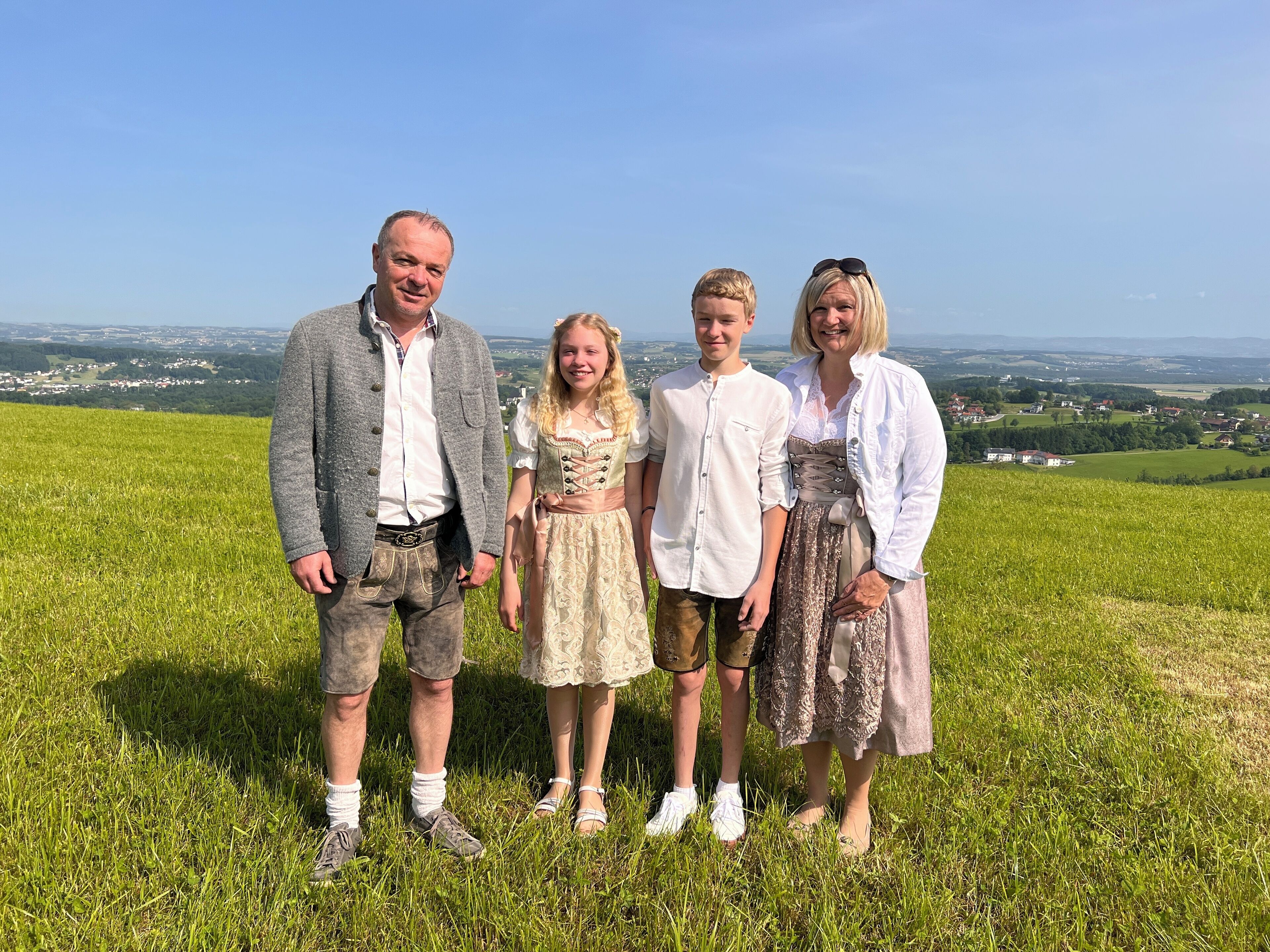 Una familia parada en una colina cubierta de hierba, con una vista panorámica de un valle y casas al fondo.