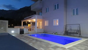 En moderne bygning med swimmingpool, overdækket terrasse og gyngestativ.