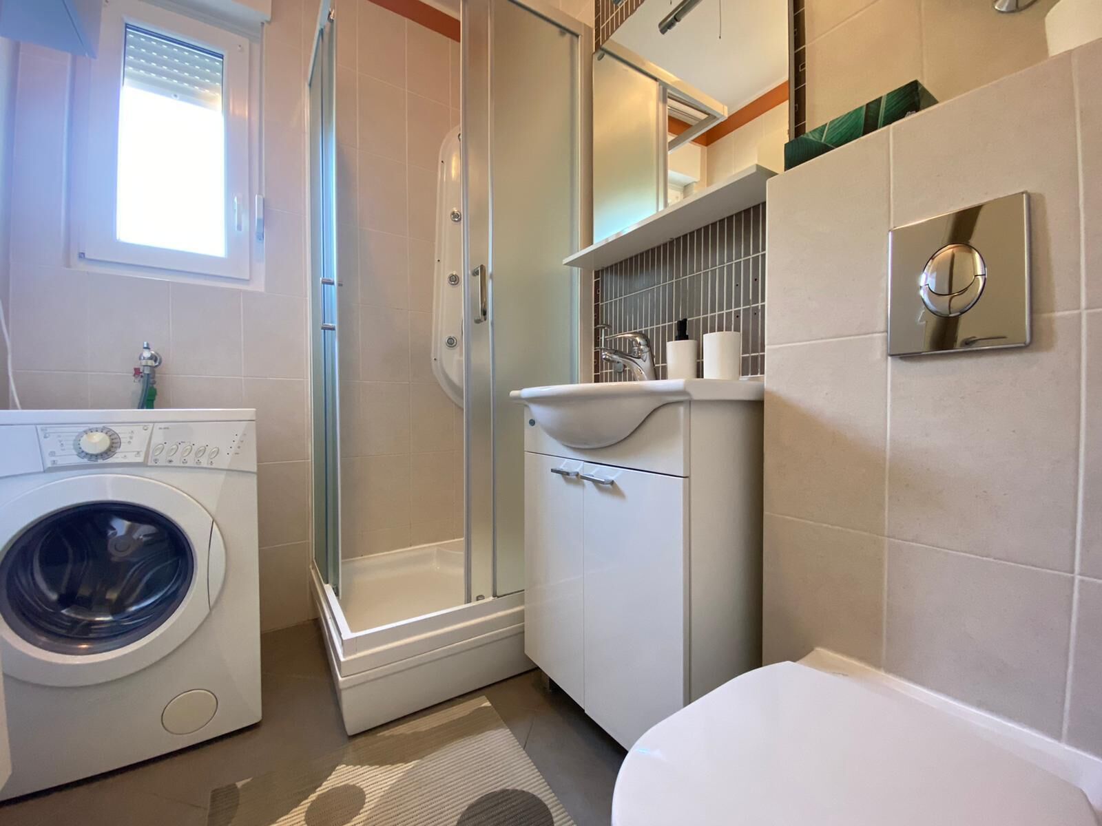 Un baño pequeño con lavadora, cabina de ducha y retrete.