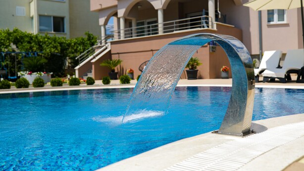 A swimming pool with a water feature, surrounded by a building with balconies and outdoor seating.