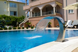 A swimming pool with a water feature, surrounded by a building with balconies and outdoor seating.