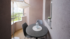 A small balcony with a round table and two chairs, a white umbrella, and a potted plant.