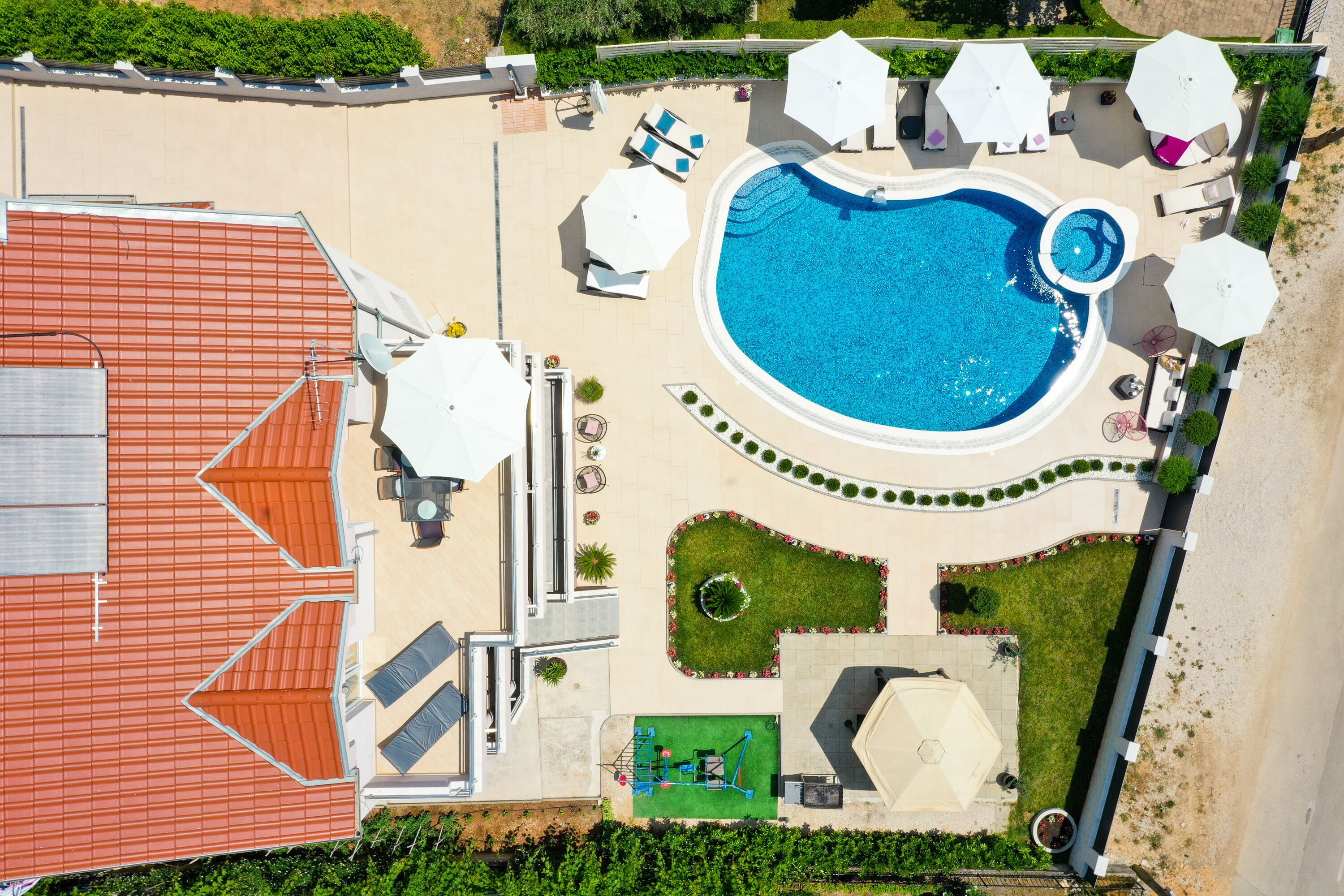 Eine Luftaufnahme eines Resorts mit Schwimmbad, Liegestühlen und Tennisplatz.