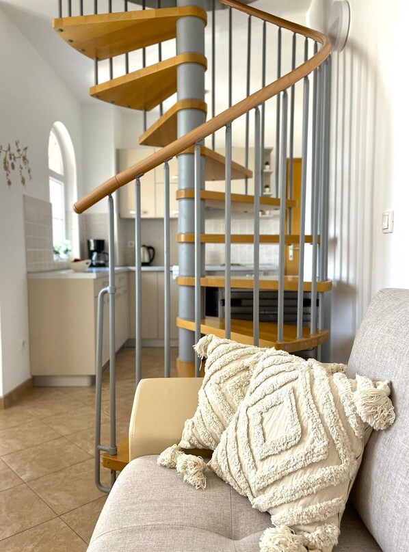 A modern interior with a spiral staircase, a kitchen area, and a cozy seating area with a textured throw pillow.