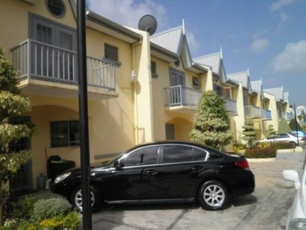 A row of yellow two-story townhouses with balconies, a black car parked in front, and a clear sky.