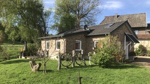 Una casa de piedra con techo inclinado, un patio cubierto de césped y un carretón de madera.