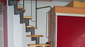 Una escalera con escalones de madera y barandillas de metal que lleva a una puerta roja.