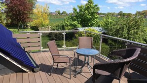 Eine Terrasse mit Korbstühlen und einem kleinen Tisch, mit Blick auf eine grüne Landschaft mit Bäumen und einem Haus.