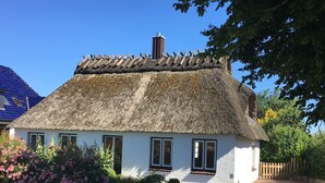 Ein traditionelles reetgedecktes Häuschen mit weißer Fassade, einem Ziegelweg, der zum Eingang führt, und einem Garten mit rosa Blumen.