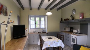 Una cocina compacta con mesa, sillas, televisor y electrodomésticos básicos.
