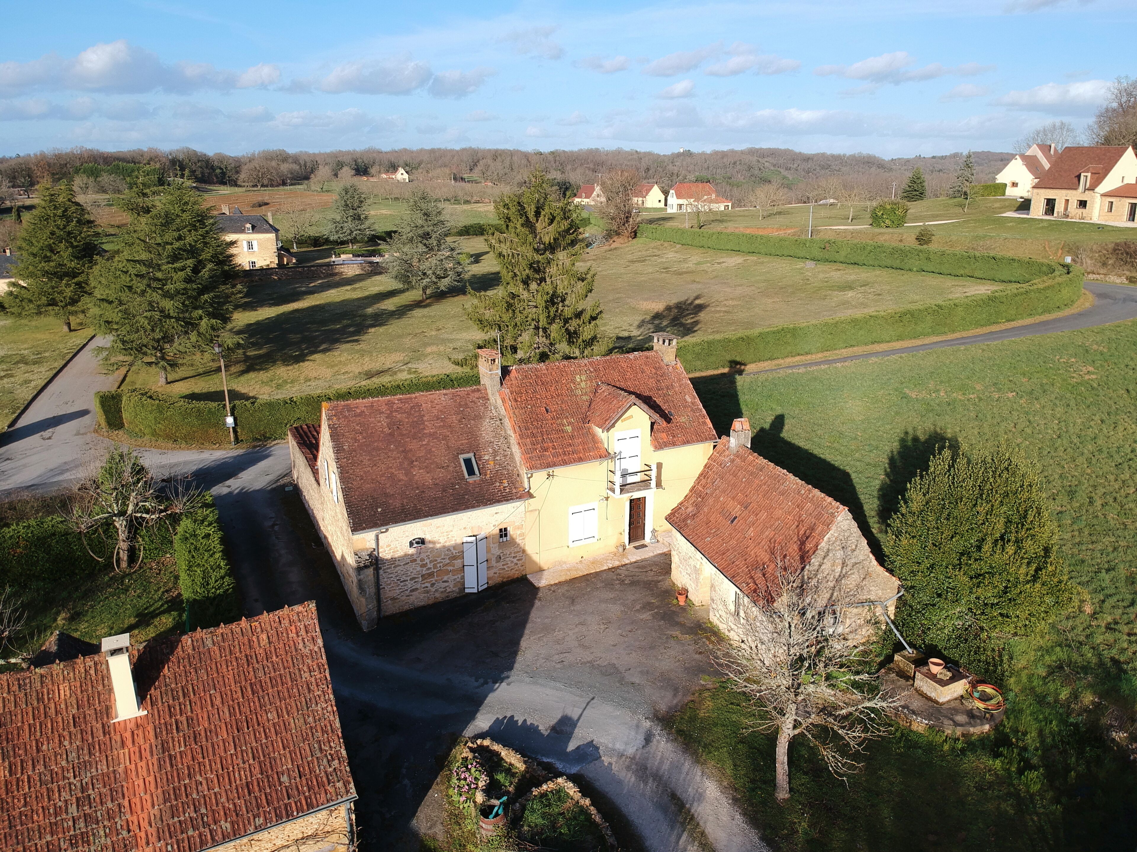 Une maison de campagne avec une façade en pierre, un toit recouvert de tuiles rouges et un petit jardin devant, avec un chemin menant à l’entrée.