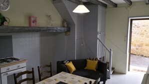 Una cocina acogedora con comedor, que incluye una mesa con mantel acolchado, sillas de madera, una estufa y una lámpara colgante.