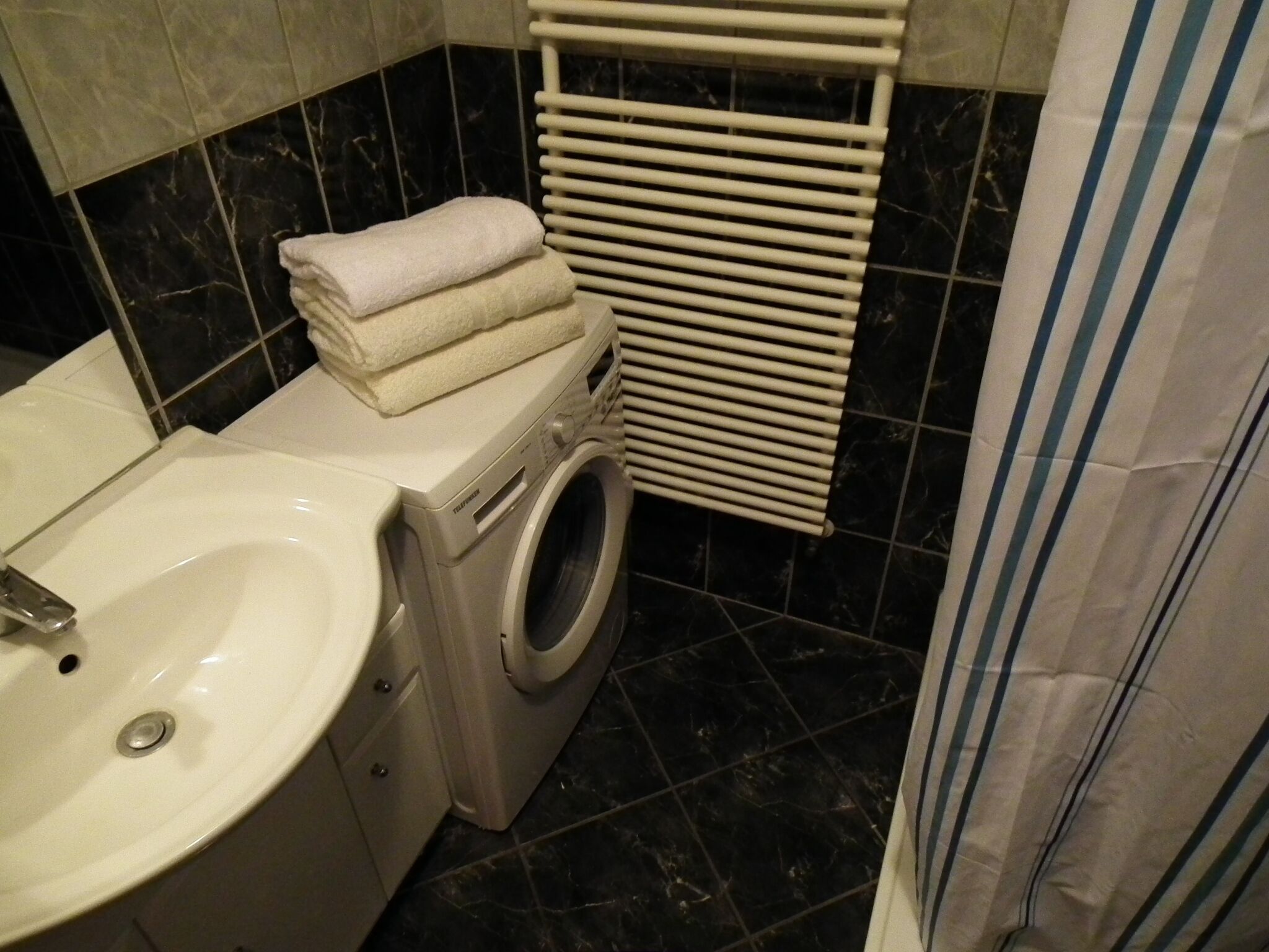 Ein kleines Badezimmer mit einem weißen Waschbecken, einer Waschmaschine und einem Handtuchhalter.