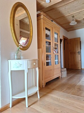 A room with a wooden floor, a white console table with a mirror, a wooden cabinet with glass doors, and a ceiling fan.