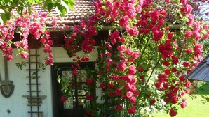 A rustic building with a door and a garden with blooming pink roses. - Heissbauer Vacation Rental "Rosentraum" with Mountain Views and Two Bedrooms (Wackersberg)