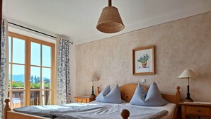 A wooden bed with a headboard, two bedside tables with lamps, a window with curtains, and a framed picture on the wall. - Heissbauer Vacation Rental "Rosentraum" with Mountain Views and Two Bedrooms (Wackersberg)