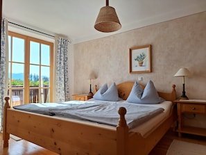 A wooden bed with a headboard, two bedside tables with lamps, a window with curtains, and a framed picture on the wall.