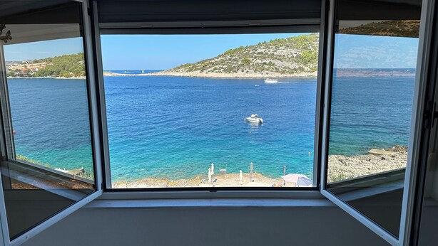 A room with a large window offering a view of a coastal area with boats and rocky terrain. - Directly by the sea, A4 - Penthouse apartment, 180m², 8 pers. (Razanj)
