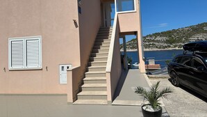 A building with a staircase leading to a balcony, a car parked nearby, and a view of the sea. - Directly by the sea, A4 - Penthouse apartment, 180m², 8 pers. (Razanj)