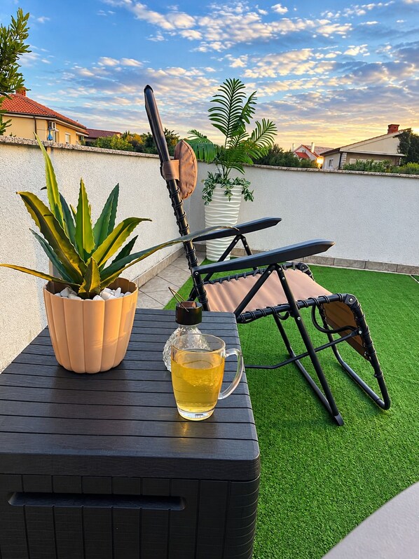 A patio with a black folding chair, a potted plant, and a glass bottle of liquid.