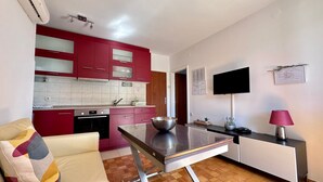 A compact living space with a kitchenette, a sofa, a dining table, and a TV mounted on the wall. - Apartment Sonja with a great terrace, near the beach, close to center (Krk)