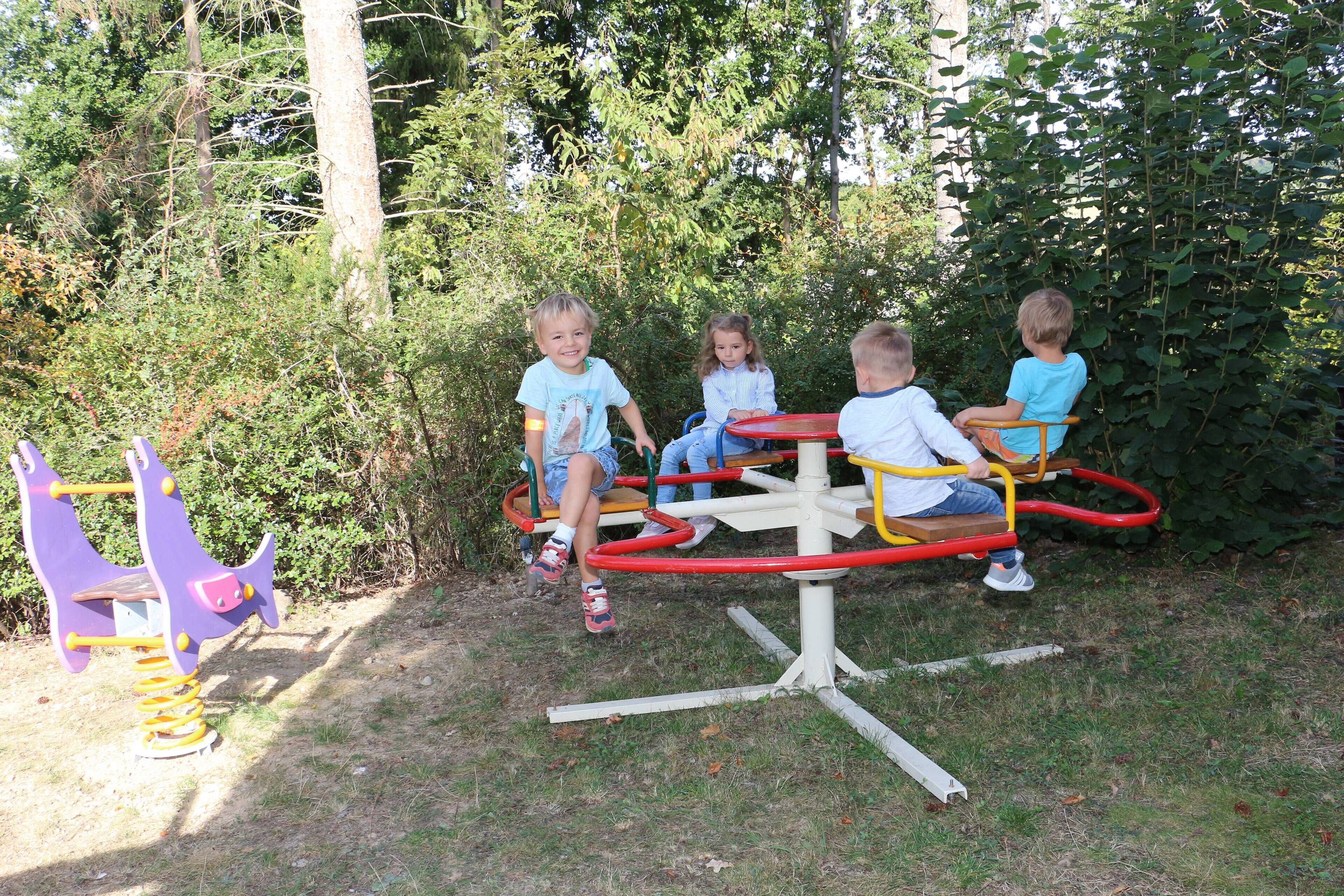 Children playing on a playground with a seesaw and a merry-go-round.