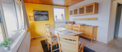 Una cocina moderna con armarios de madera, una mesa de comedor con sillas y un amplio ventanal que proporciona luz natural.