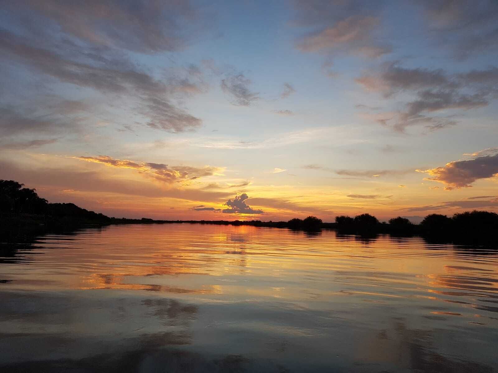A calm lake at sunset with a clear sky and distant trees.