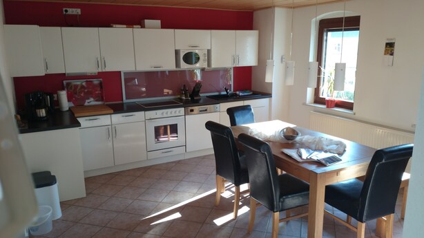 Een compacte keuken met witte kastjes, een magnetron, een oven en een eethoek met een tafel en stoelen.