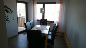 Een eetgedeelte met een tafel, stoelen en een raam met gordijnen.