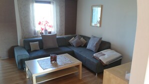 Een woonkamer met een grijze bank, een houten salontafel en een raam met gordijnen.