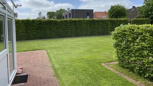 Een verzorgd gazon met een pad van baksteen dat naar een deur leidt, omringd door een hoge haag en een keurig bijgesnoeide struik.