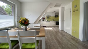 Een moderne keuken met witte kasten, een groene accentmuur en een eetgedeelte met een houten tafel en witte stoelen.