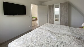 Een slaapkamer met een bed, een televisie aan de muur en een deur naar een andere kamer.