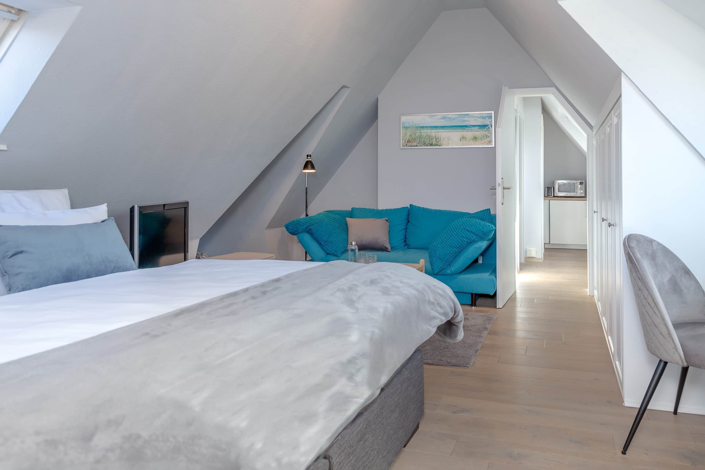 Une chambre à coucher avec un lit, un canapé, une lampe et une vue sur une cuisine par une porte ouverte.